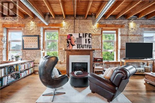 Living room with a wood ceiling with exposed beams, wood finished floors, plenty of natural light, and a glass covered fireplace - 25 Concession Street Unit# 201, Cambridge, ON - Indoor With Fireplace