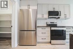 Kitchen showcasing stainless steel refrigerator, white cabinetry with dark hardware, black electric range with coordinating microwave, and subway tile backsplash - 