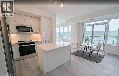 Kitchen featuring stainless steel appliances, white cabinets, light wood-style floors, backsplash, and a kitchen island - 385 Winston Road Unit# 1311, Grimsby, ON - Indoor Photo Showing Kitchen