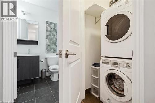 Laundry area featuring stacked washer and dryer and dark tile patterned flooring - 40 Esplanade Lane Unit# 102, Grimsby, ON - Indoor Photo Showing Laundry Room