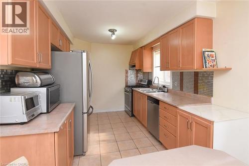 Kitchen featuring decorative backsplash, stainless steel appliances, light countertops, light tile patterned floors, and light wood finish cabinetry - 142 Hawkswood Trail, Hamilton, ON - Indoor Photo Showing Kitchen With Double Sink
