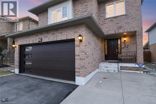 Exterior entry at dusk with an attached garage, asphalt driveway, and brick siding - 142 Hawkswood Trail, Hamilton, ON - Outdoor With Exterior