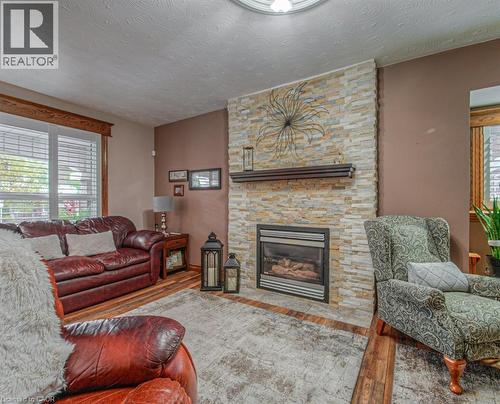 Living area featuring healthy amount of natural light, a textured ceiling, wood finished floors, and a stone fireplace - 81 Beechwood Avenue, Hamilton, ON - Indoor Photo Showing Living Room With Fireplace
