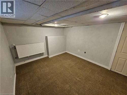 Finished basement featuring dark carpet, radiator heating unit, and a drop ceiling - 170 Stewartdale Avenue, Hamilton, ON - Indoor