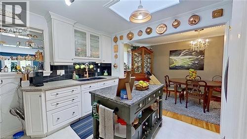 Kitchen with white cabinets, decorative backsplash, ornamental molding, glass fronted cabinets, and light stone countertops - 27 Hepburn Avenue, St. Thomas, ON - Indoor Photo Showing Kitchen