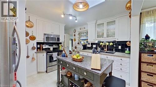 Dual tone kitchen with open shelves, stainless steel appliances, glass insert cabinets, tasteful backsplash, and dark stone countertops - 27 Hepburn Avenue, St. Thomas, ON - Indoor Photo Showing Kitchen