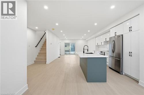 Kitchen with stainless steel appliances, an island with sink, light wood-type flooring, dual tone cabinetry, and backsplash - 1278 Main Street E, Hamilton, ON - Indoor Photo Showing Kitchen With Upgraded Kitchen