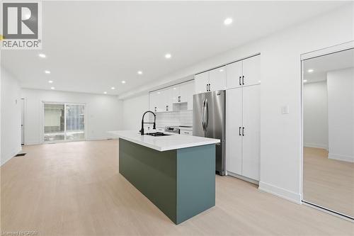 Kitchen featuring stainless steel appliances, light wood finished floors, a center island with sink, tasteful backsplash, and two tone cabinetry - 1278 Main Street E, Hamilton, ON - Indoor