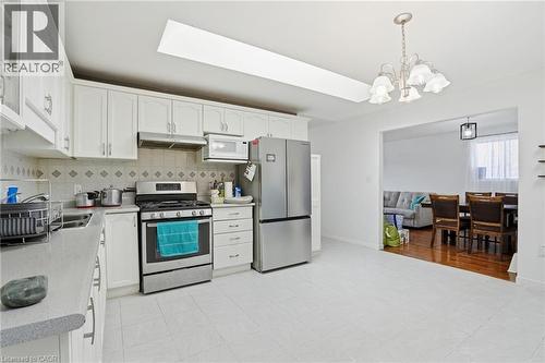 Kitchen with stainless steel appliances, white cabinets, hanging lights, backsplash, and a skylight - 513 Rexford Drive, Hamilton, ON - Indoor Photo Showing Kitchen