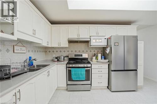 Kitchen with stainless steel appliances, white cabinets, light countertops, light tile patterned floors, and backsplash - 513 Rexford Drive, Hamilton, ON - Indoor Photo Showing Kitchen With Double Sink