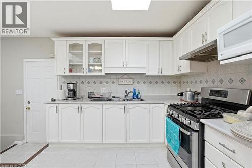 Kitchen featuring stainless steel gas stove, white microwave, light countertops, glass fronted cabinets, and white cabinets - 513 Rexford Drive, Hamilton, ON - Indoor Photo Showing Kitchen With Double Sink