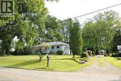 View of front of house featuring a front lawn, gravel driveway, and view of scattered trees - 