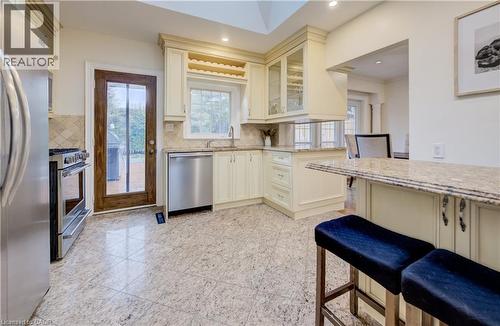 Kitchen with stainless steel appliances, light stone countertops, glass insert cabinets, granite tiled floors, and cream cabinetry - 655 Ellengale Road, Burlington, ON - Indoor Photo Showing Kitchen