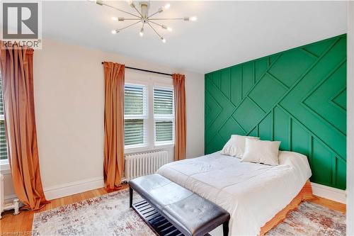 Bedroom featuring an accent wall, radiator, light wood-style flooring, and a chandelier - 134 Sherman Avenue S, Hamilton, ON - Indoor Photo Showing Bedroom