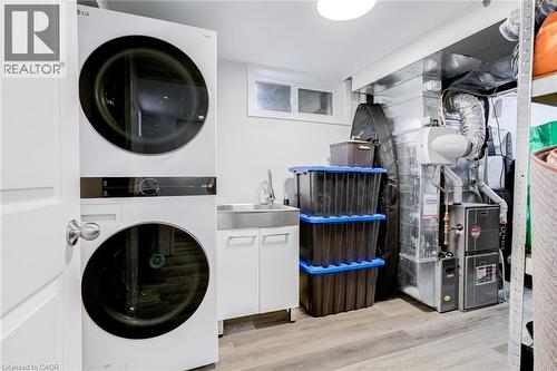 Laundry area featuring stacked washer / drying machine, light wood-type flooring, and heating unit - 624 Burgess Avenue, Hamilton, ON - Indoor Photo Showing Laundry Room