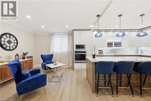 Two tone kitchen with light wood-type flooring, stainless steel appliances, decorative backsplash, a breakfast bar, and hanging light fixtures - 273 Bryant Crescent, Burlington, ON - Indoor Photo Showing Other Room