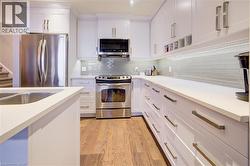 Kitchen with appliances with stainless steel finishes, white cabinetry, decorative backsplash, light wood-type flooring, and open shelves - 