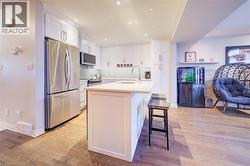 Kitchen with appliances with stainless steel finishes, white cabinets, a kitchen breakfast bar, a kitchen island with sink, and light wood-type flooring - 
