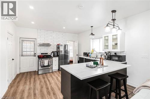 Kitchen featuring a peninsula, a kitchen breakfast bar, light countertops, glass insert cabinets, and stainless steel appliances - 57 New Street, Hamilton, ON - Indoor
