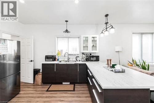 Kitchen with a peninsula, freestanding refrigerator, hanging light fixtures, glass fronted cabinets, and light wood-type flooring - 57 New Street, Hamilton, ON - Indoor Photo Showing Other Room
