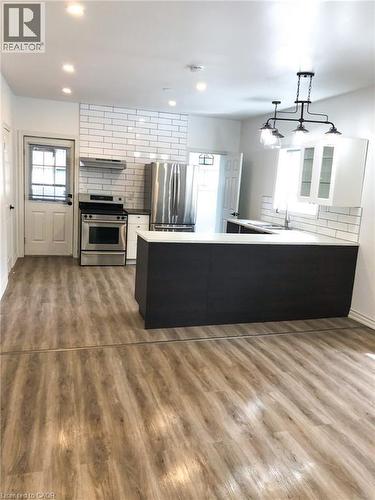 Dual tone kitchen featuring a peninsula, stainless steel appliances, healthy amount of natural light, tasteful backsplash, and dual tone cabinets - 57 New Street, Hamilton, ON - Indoor Photo Showing Kitchen With Fireplace
