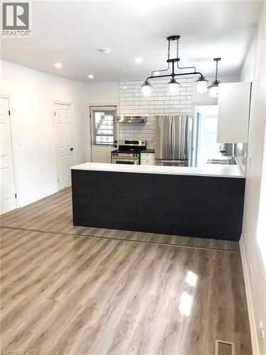 Kitchen featuring a peninsula, light countertops, stainless steel appliances, light wood-type flooring, and decorative light fixtures - 57 New Street, Hamilton, ON - Indoor Photo Showing Kitchen