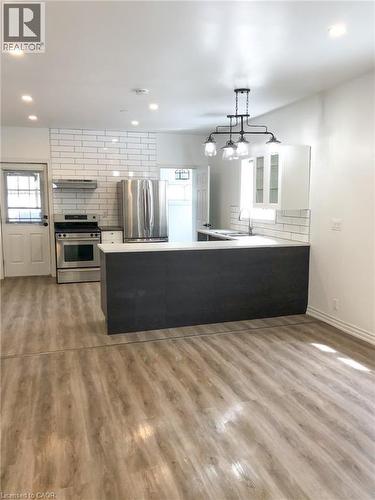 Kitchen with a peninsula, stainless steel appliances, backsplash, decorative light fixtures, and light wood finished floors - 57 New Street, Hamilton, ON - Indoor Photo Showing Kitchen