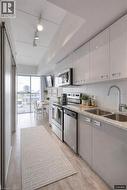Kitchen with stainless steel appliances, light stone counters, light wood-style flooring, modern cabinets, and dual tone cabinetry - 