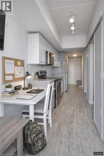 Kitchen with stainless steel appliances, a peninsula, a kitchen bar, light wood finished floors, and light stone counters - 257 Hemlock Street Unit# 607, Waterloo, ON - Indoor Photo Showing Kitchen