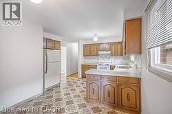 Kitchen featuring light countertops, white appliances, a peninsula, wood finish cabinetry, and light flooring - 