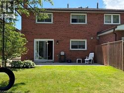 Brick exterior featuring multiple windows, a sliding glass door, a concrete patio, a privacy fence, and a green lawn - 