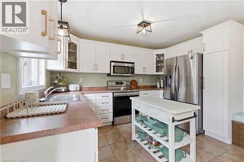 Kitchen featuring glass insert cabinets, stainless steel appliances, white cabinetry, hanging light fixtures, and light tile patterned floors - 84 Duncairn Crescent, Hamilton, ON - Indoor Photo Showing Kitchen With Double Sink