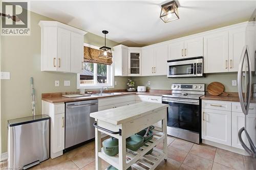 Kitchen featuring stainless steel appliances, white cabinetry, glass insert cabinets, hanging light fixtures, and light tile patterned floors - 84 Duncairn Crescent, Hamilton, ON - Indoor Photo Showing Kitchen With Double Sink