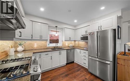 Kitchen featuring stainless steel appliances, dark stone countertops, extractor fan, dark wood-style floors, and white cabinets - 4516 Gullfoot Circle, Mississauga, ON - Indoor Photo Showing Kitchen