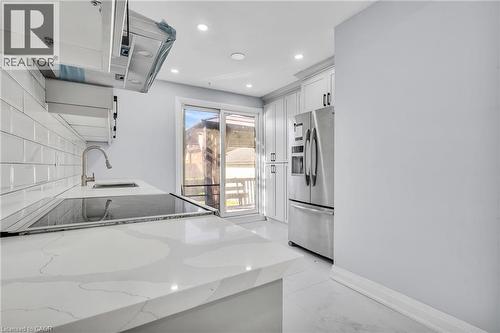 Kitchen featuring light stone countertops, ventilation hood, stainless steel fridge with ice dispenser, white cabinetry, and recessed lighting - 84 Avalon Place, Kitchener, ON - Indoor