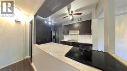 Kitchen featuring black electric cooktop, stainless steel refrigerator with ice dispenser, dark wood finish cabinets, decorative backsplash, and a peninsula - 