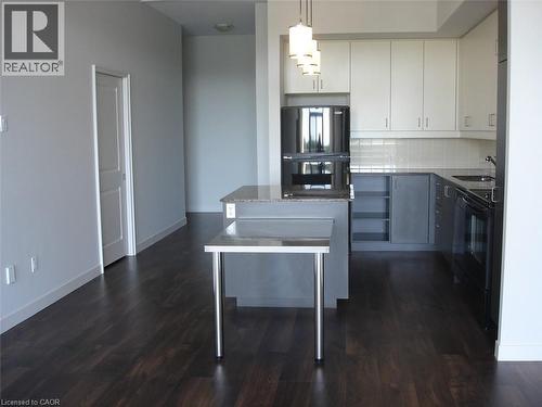 Dual tone kitchen featuring black appliances, hanging light fixtures, decorative backsplash, two tone color scheme, and light stone counters - 191 King Street S Unit# 712, Waterloo, ON - Indoor Photo Showing Kitchen