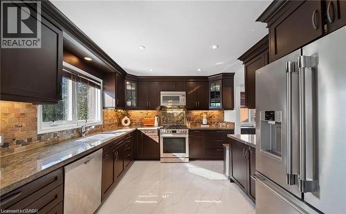 Kitchen featuring high end appliances, dark wood finish cabinetry, dark stone countertops, light marble finish floors, and recessed lighting - 1550 Woodeden Drive, Mississauga, ON - Indoor Photo Showing Kitchen With Double Sink With Upgraded Kitchen