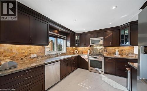 Kitchen featuring light stone counters, stainless steel appliances, dark wood finish cabinetry, light marble finish flooring, and glass insert cabinets - 1550 Woodeden Drive, Mississauga, ON - Indoor Photo Showing Kitchen With Double Sink With Upgraded Kitchen
