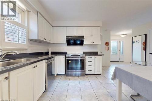 Kitchen featuring stainless steel appliances, white cabinets, dark countertops, and light tile patterned flooring - 62 Como Place, Hamilton, ON - Indoor Photo Showing Kitchen With Double Sink