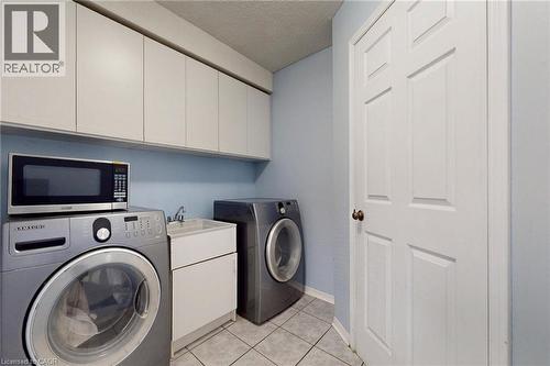 Laundry area with washer and dryer, a textured ceiling, cabinet space, and light tile patterned flooring - 62 Como Place, Hamilton, ON - Indoor Photo Showing Laundry Room