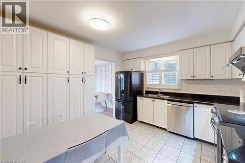 Kitchen featuring stainless steel appliances, white cabinetry, backsplash, light tile patterned floors, and dark stone countertops - 62 Como Place, Hamilton, ON - Indoor Photo Showing Kitchen