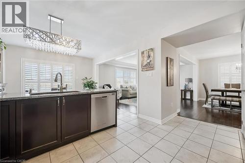 Kitchen with suspended lighting, dark wood finish cabinetry, stainless steel dishwasher, dark stone countertops, and light tile patterned flooring - 38 Park Glen Street, Kitchener, ON - Indoor