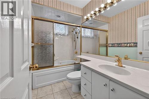 Bathroom with vanity, light tile patterned floors, bath / shower combo with glass door, and wallpapered walls - 21 Bluebird Avenue, Hamilton, ON - Indoor Photo Showing Bathroom