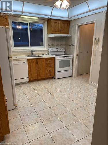 Kitchen featuring wood cabinetry, white appliances, and tiled flooring - 21 Bluebird Avenue, Hamilton, ON 
