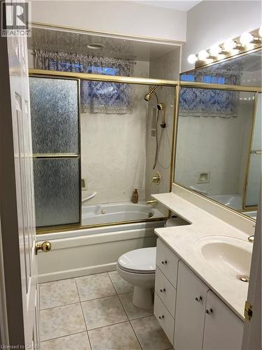 Full bathroom featuring a tub/shower combination with a gold-toned framed enclosure, a single vanity with storage cabinetry, and tiled flooring - 21 Bluebird Avenue, Hamilton, ON 