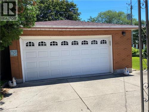 Attached two-car garage featuring a white panel door with arched window inserts, brick exterior, and a shingle roof - 21 Bluebird Avenue, Hamilton, ON 