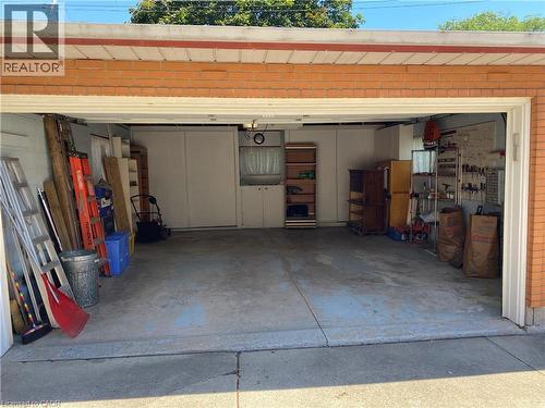 Attached two-car garage with a concrete floor, brick exterior, and built-in shelving and cabinetry for organized storage - 21 Bluebird Avenue, Hamilton, ON 