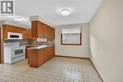 Kitchen featuring white appliances, wood finish cabinetry, a peninsula, backsplash, and light flooring - 122 Glen Forest Drive, Hamilton, ON - Indoor Photo Showing Kitchen