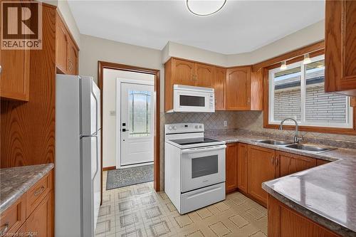 Kitchen with white appliances, light floors, wood finish cabinets, decorative backsplash, and dark countertops - 122 Glen Forest Drive, Hamilton, ON - Indoor Photo Showing Kitchen With Double Sink